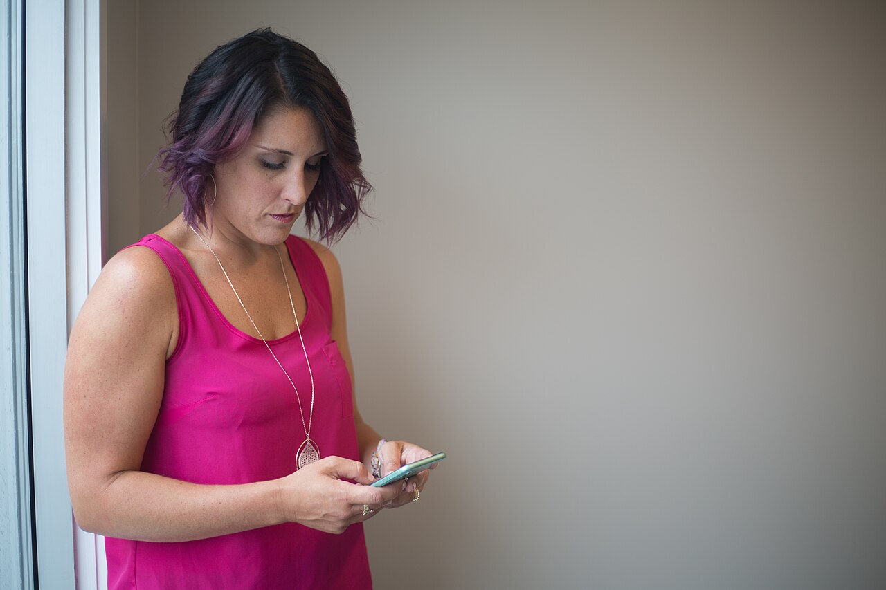 Mulher usando um celular perto de uma janela.
