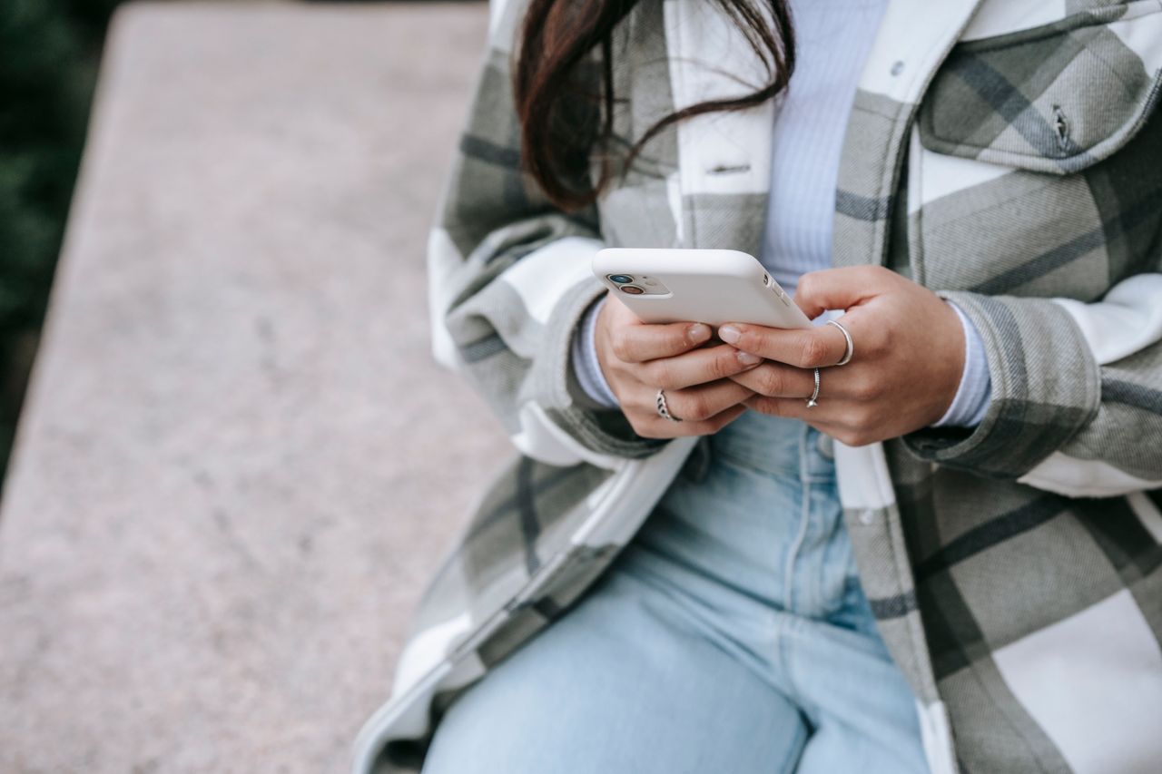 Pessoa sentada ao ar livre usando um celular com as duas mãos; a tela não aparece.